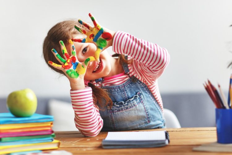happy funny child girl draws laughing shows hands dirty with paint