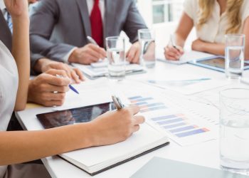 Mid section of business people writing notes in board room meeting at office