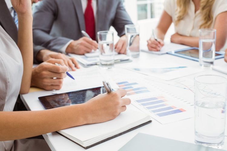 Mid section of business people writing notes in board room meeting at office