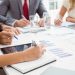 Mid section of business people writing notes in board room meeting at office